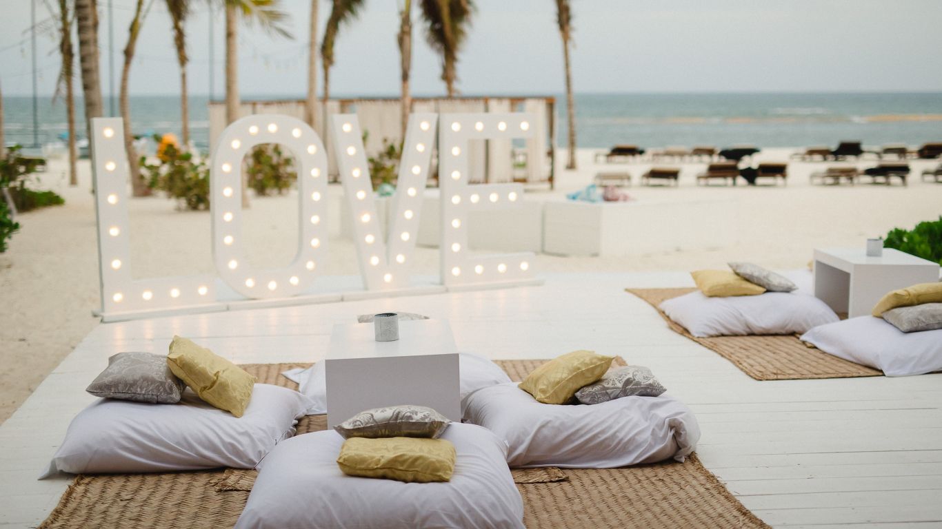LOVE sign wit lights and pillows and small tables set up on the beach